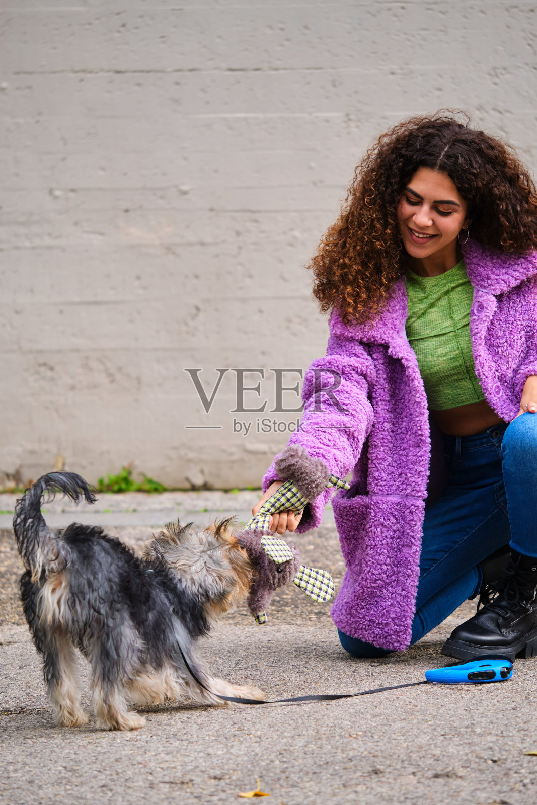年轻的西班牙女子在街上和她的约克夏梗狗玩耍。照片摄影图片