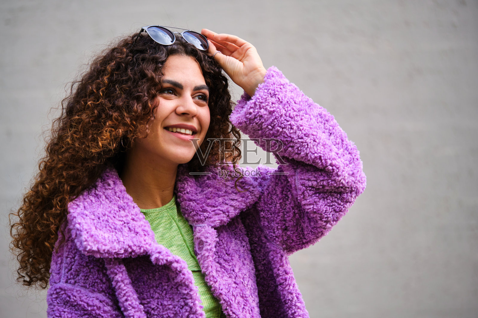 年轻的西班牙女人，卷发，紫色外套，戴着墨镜，微笑着。照片摄影图片
