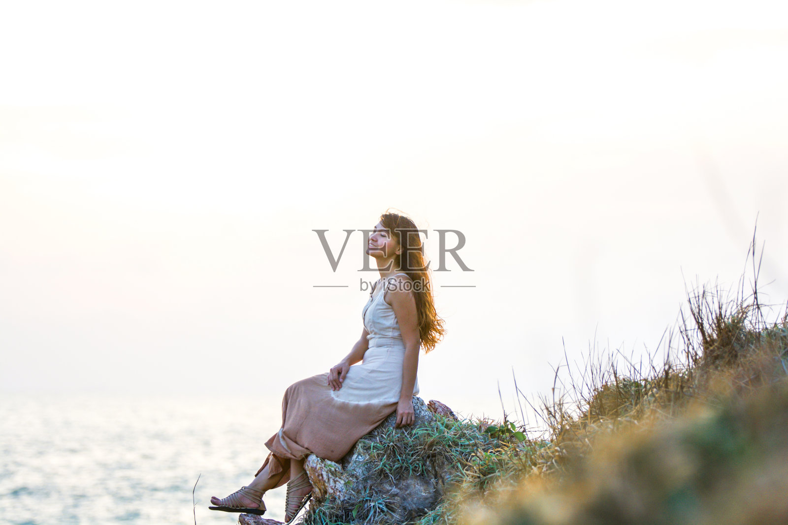 美丽的年轻亚洲女人享受海滩上的岩石。冷静，放松，微笑，心态重置概念。年轻女子坐在悬崖顶上，呼吸着新鲜空气，欣赏着海景照片摄影图片