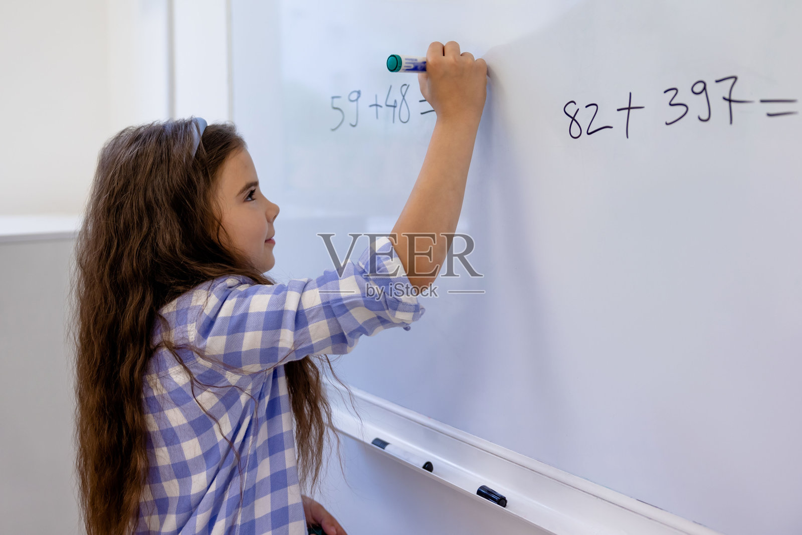 小女孩在学校的白板上计算数学方程式。照片摄影图片