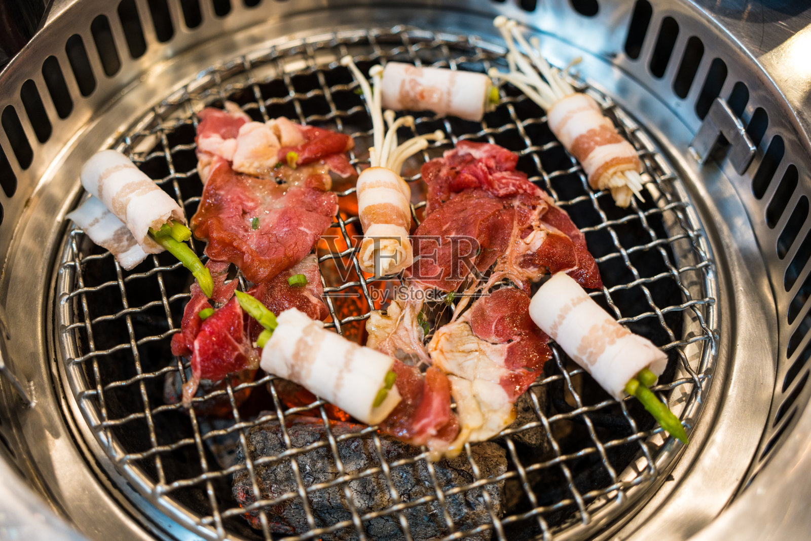 生牛肉和熏肉卷，在烧烤炉上有热木炭。照片摄影图片