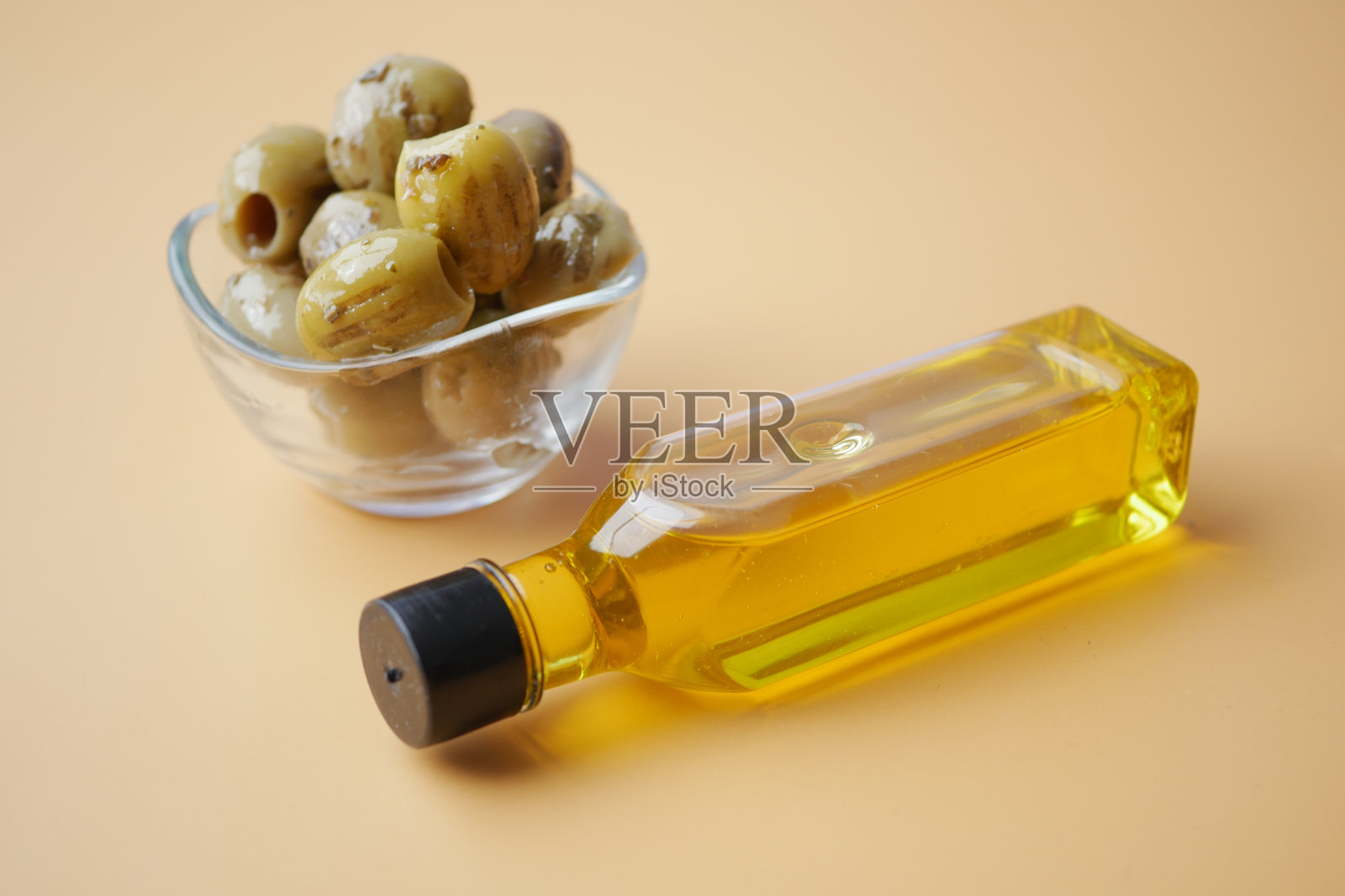 一瓶橄榄油和新鲜的橄榄油放在桌子上的容器里。照片摄影图片