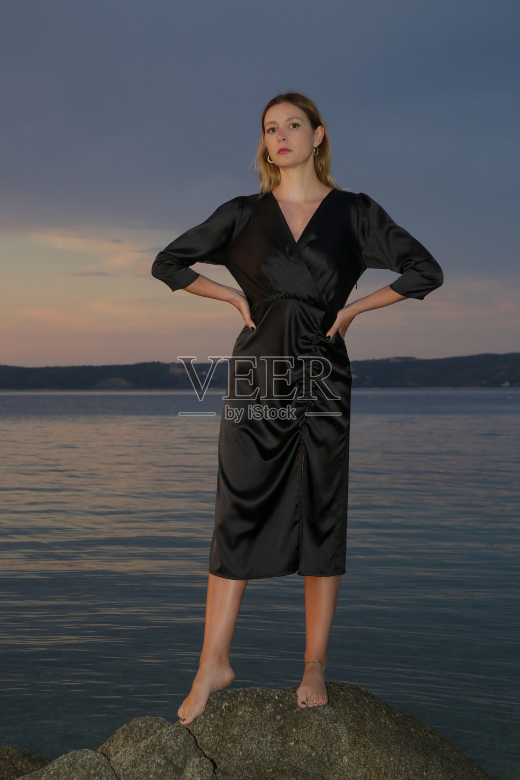 美丽的户外时尚肖像的女人在日落在海滩上的黑色连衣裙照片摄影图片