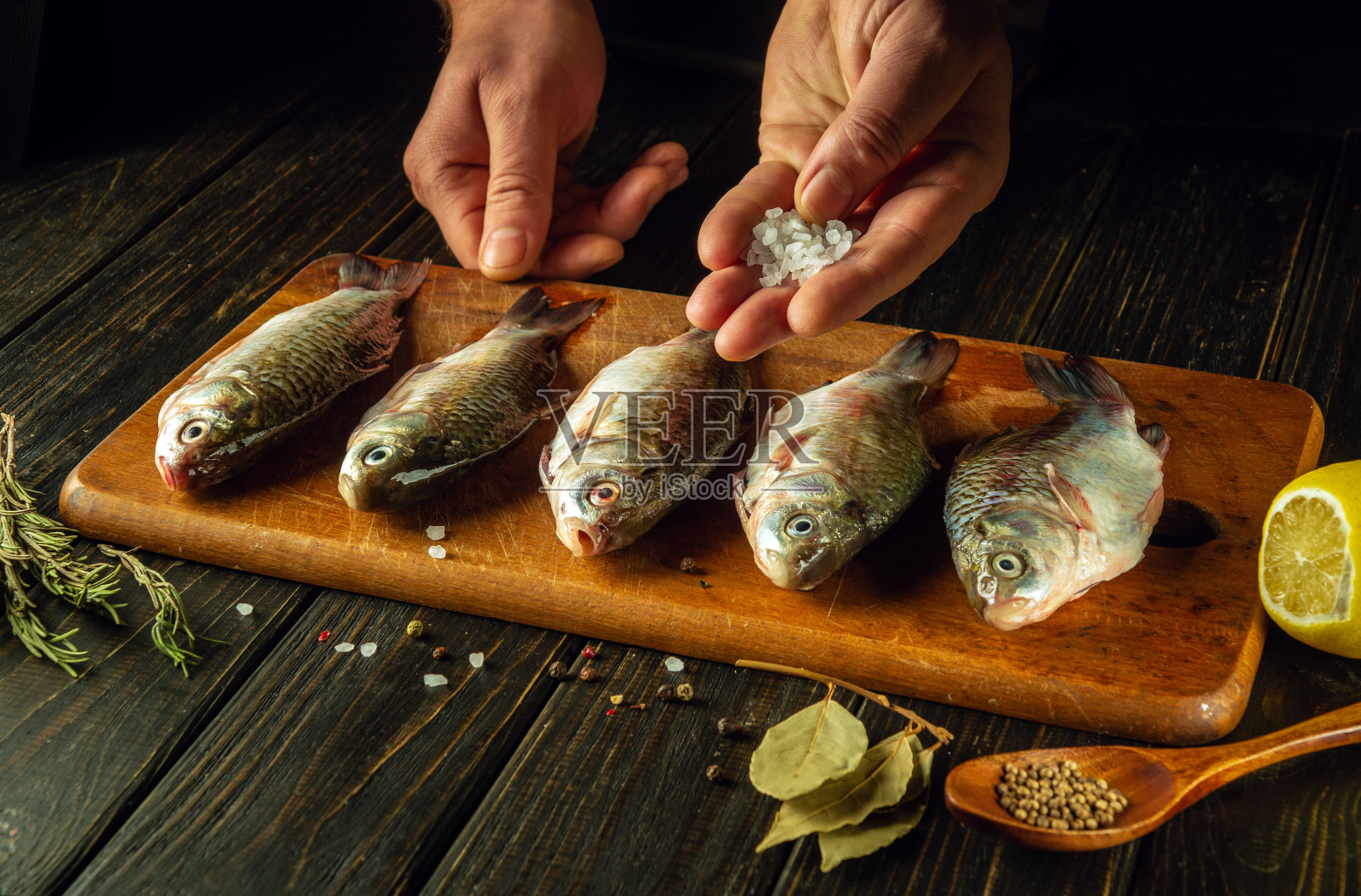 厨师用手给鲜鱼加盐。在厨房餐桌上用香料和香菜烹调鲫鱼的过程照片摄影图片