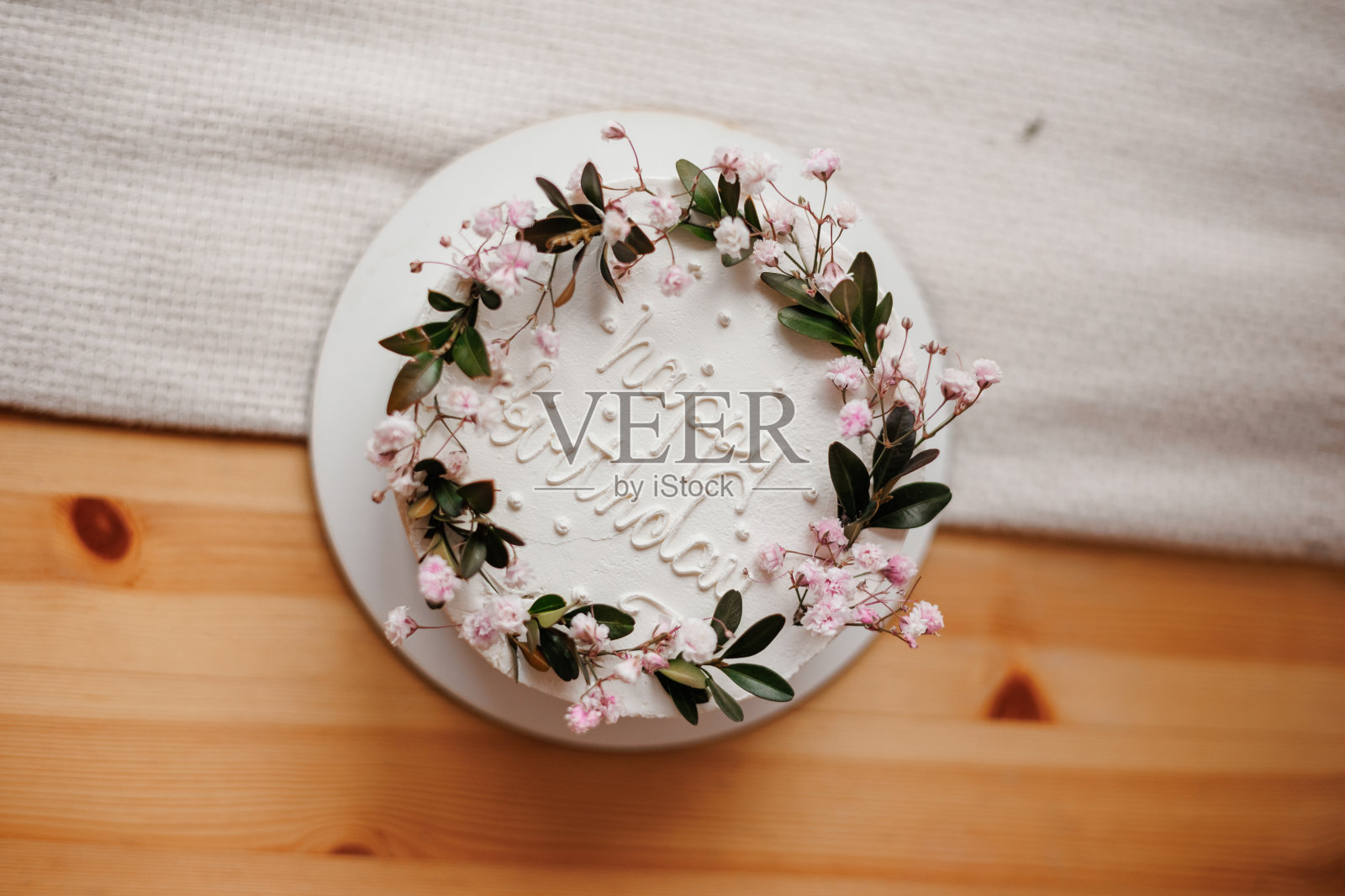 乡村风格的白色奶油蛋糕，上面装饰着鲜花，绿色和生日快乐的字样，放在天然亚麻桌布的木制桌子上。生日聚会自制甜点照片摄影图片