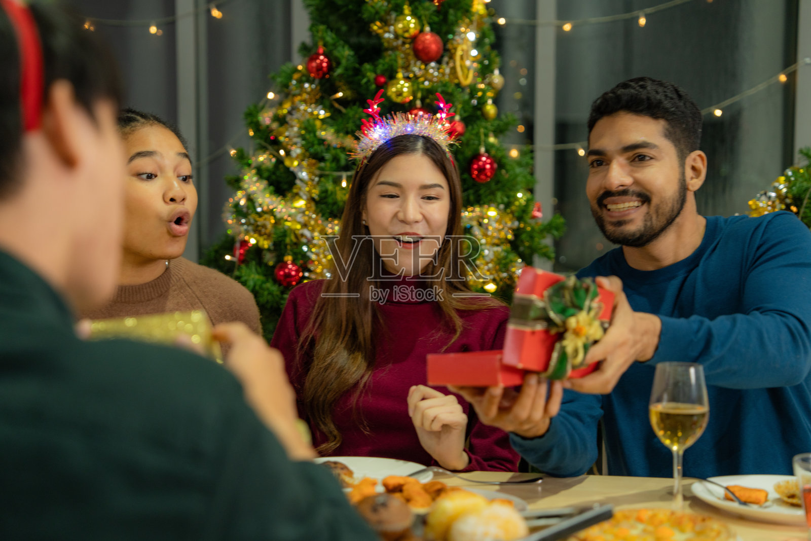 一群亚洲朋友欢度新年的圣诞晚会。朋友们一起在家里吃晚饭。男女打开礼盒，一起在家里摆放圣诞树。照片摄影图片