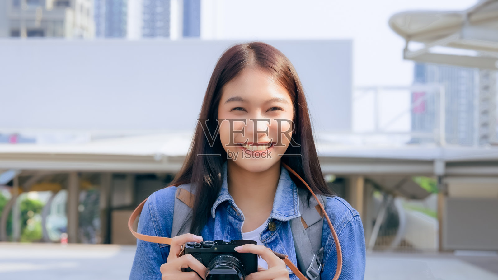 年轻的亚洲女子微笑着看着相机，女游客背着背包拿着相机照片摄影图片
