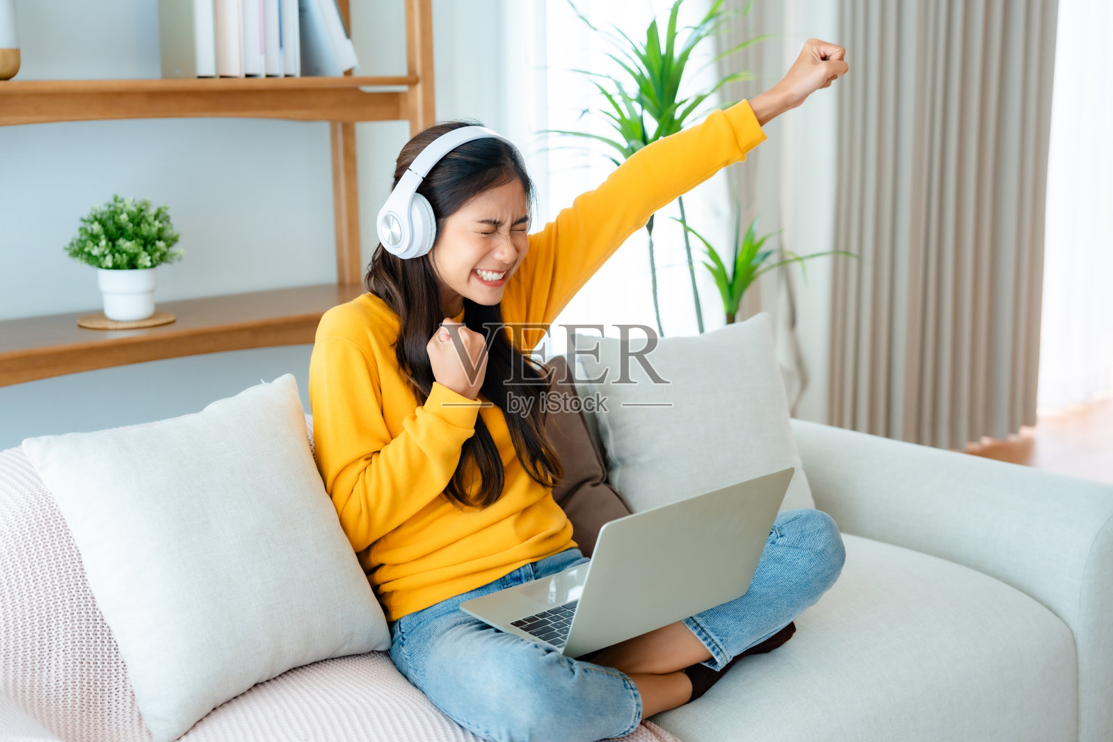 年轻快乐幸运的女学生感到兴奋获胜，使用电脑笔记本电脑，坐在沙发上，可爱的亚洲女性收到笔记本上的好消息，获得新工作庆祝成功照片摄影图片