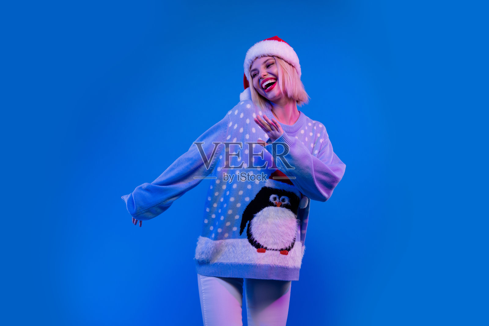 漂亮可爱的圣诞女助手穿着丑陋的印花圣诞毛衣的照片，有有趣的孤立的蓝色背景照片摄影图片
