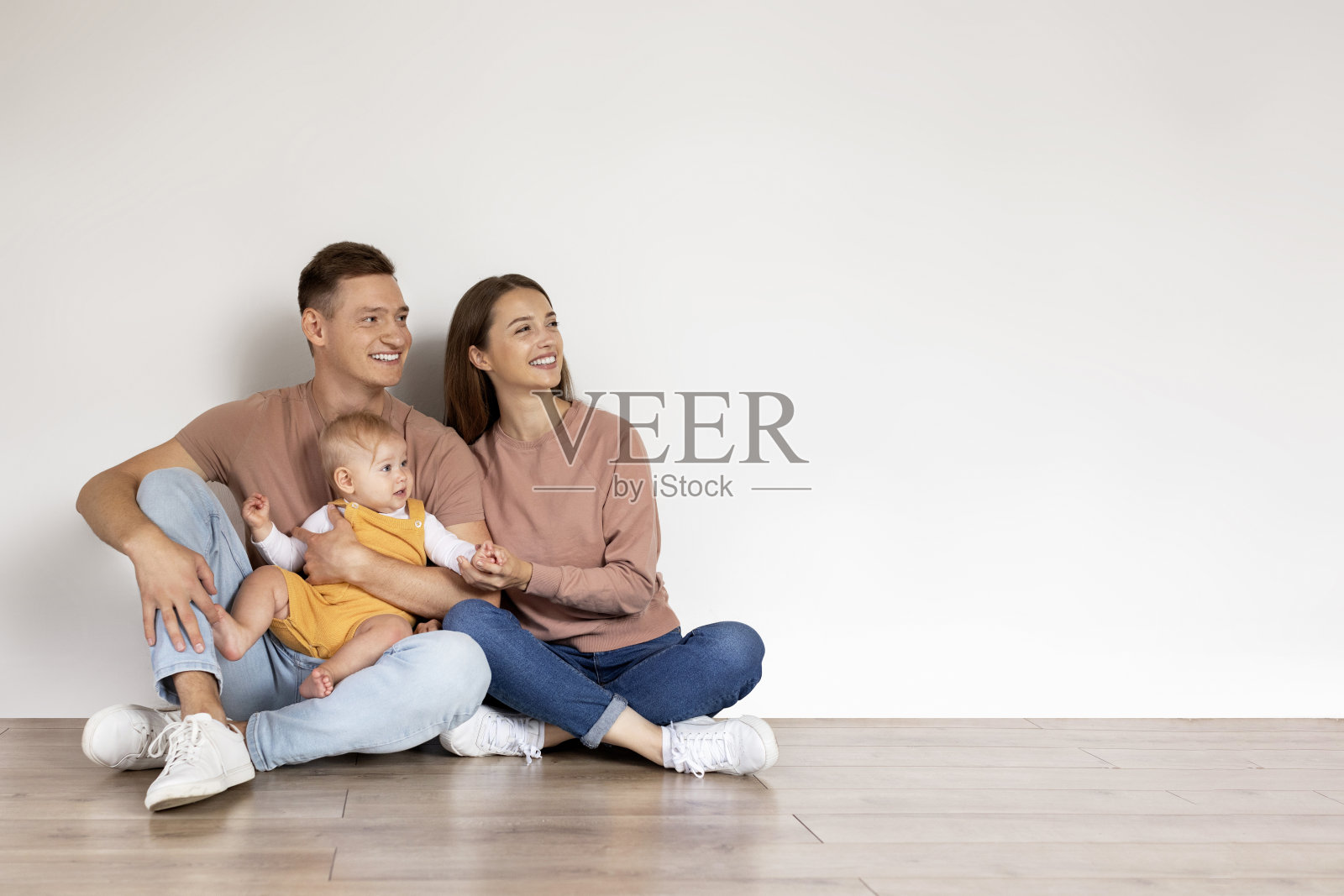 家庭提供。快乐的父母和孩子坐在地板上，看着旁边照片摄影图片