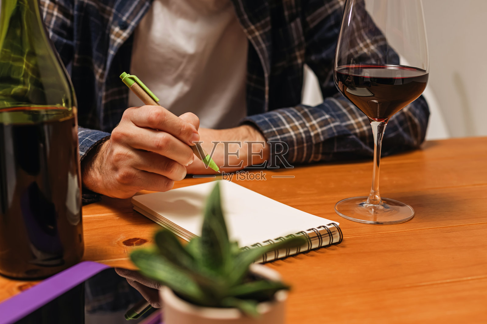一个拿着一杯酒在记事本上写东西的人，记录着酒的量或者做关于酒的笔记。照片摄影图片