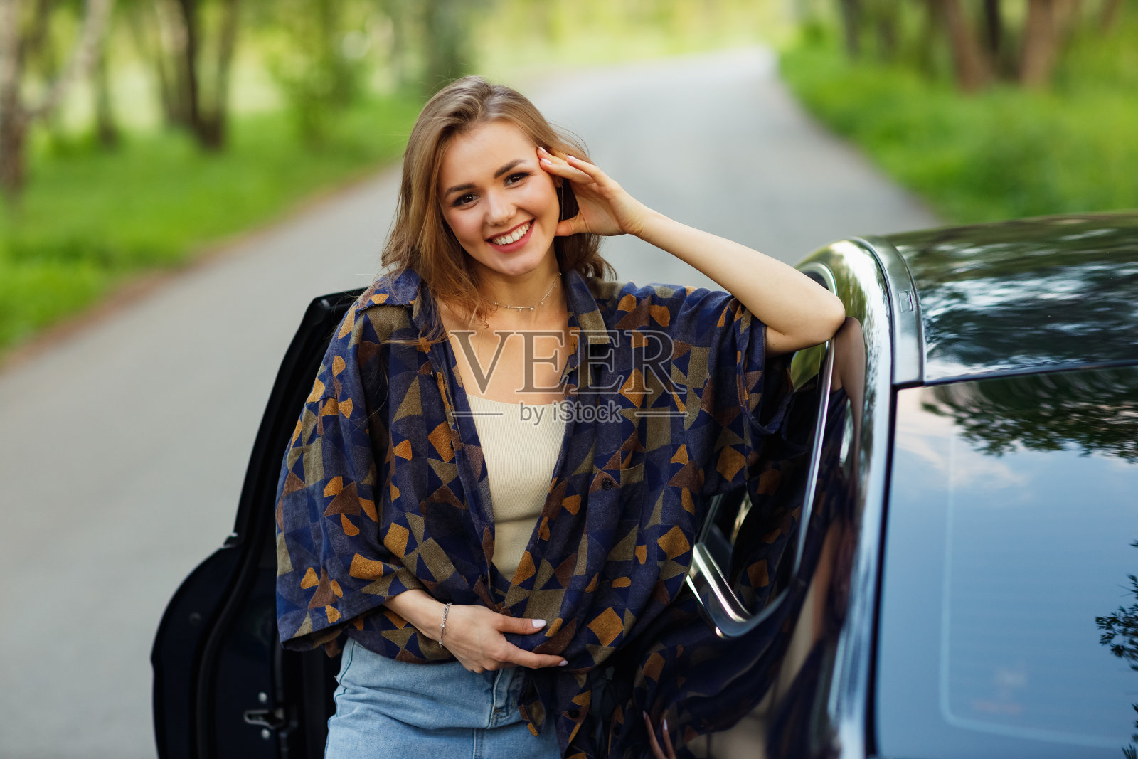 快乐的女司机微笑着看着车。可爱的年轻快乐的黑发女司机。照片摄影图片