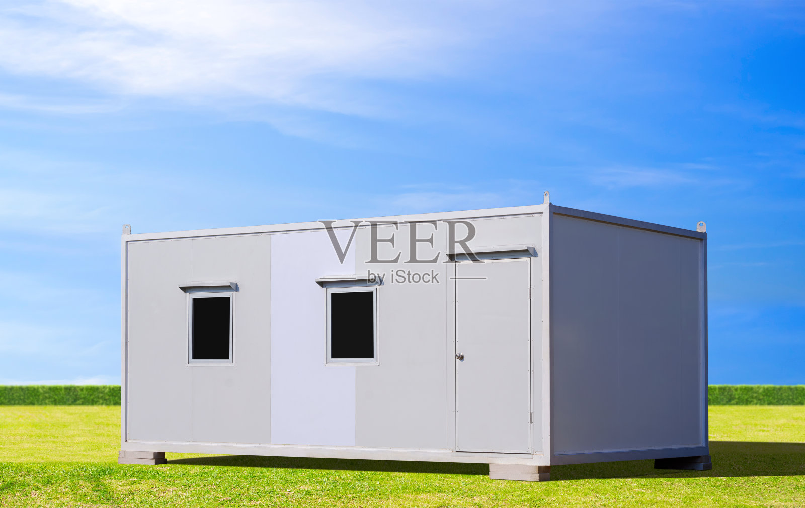 白色移动夹心板办公集装箱，在蓝天背景的绿色草坪上出租和出售照片摄影图片