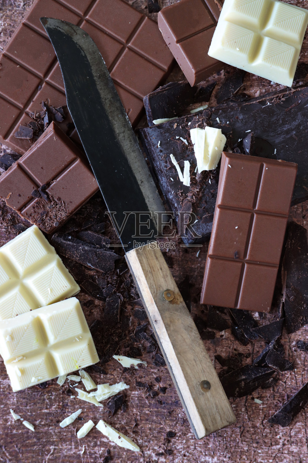 厨房刀与巧克力棒，牛奶巧克力块，白巧克力方块和黑巧克力块磨碎的棕色背景，抬高视图的特写图像照片摄影图片