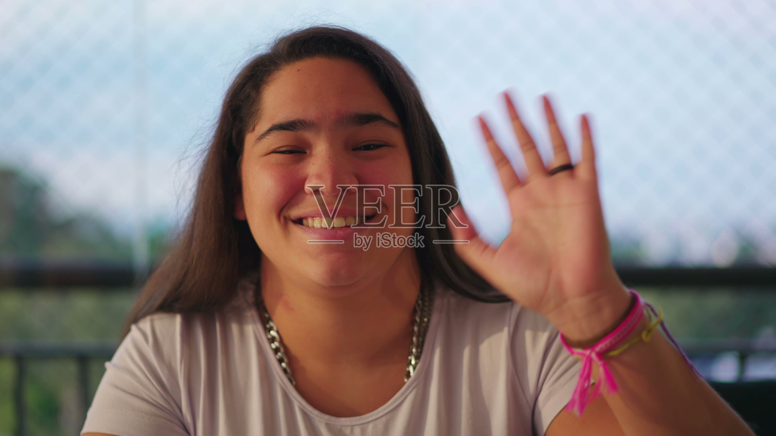 快乐的年轻女子挥手问好，并对着摄像头说话。一个不同种族的亚洲人在视频会议上讲话的肖像脸照片摄影图片