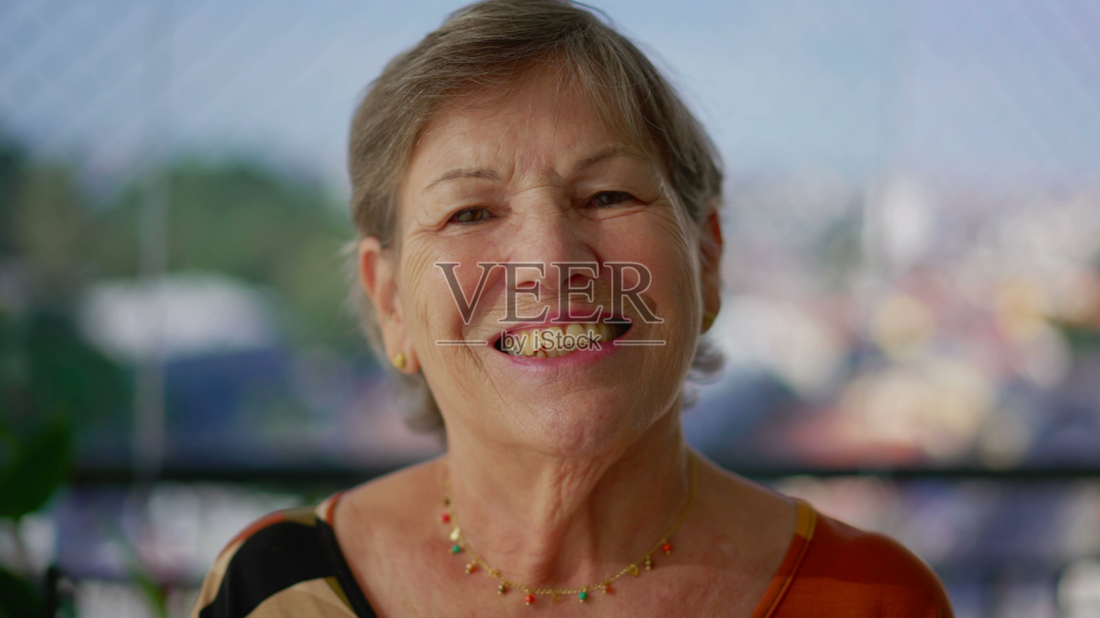 快乐的老年妇女享受城市景观，阳台肖像。在城市背景下对着镜头微笑的老妇人照片摄影图片