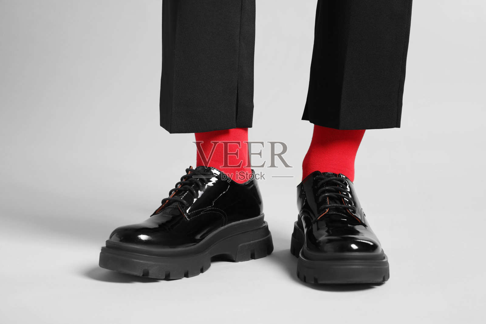 在浅灰色的背景上，穿着裤子、鞋子和时髦的红袜子的女人，特写照片摄影图片