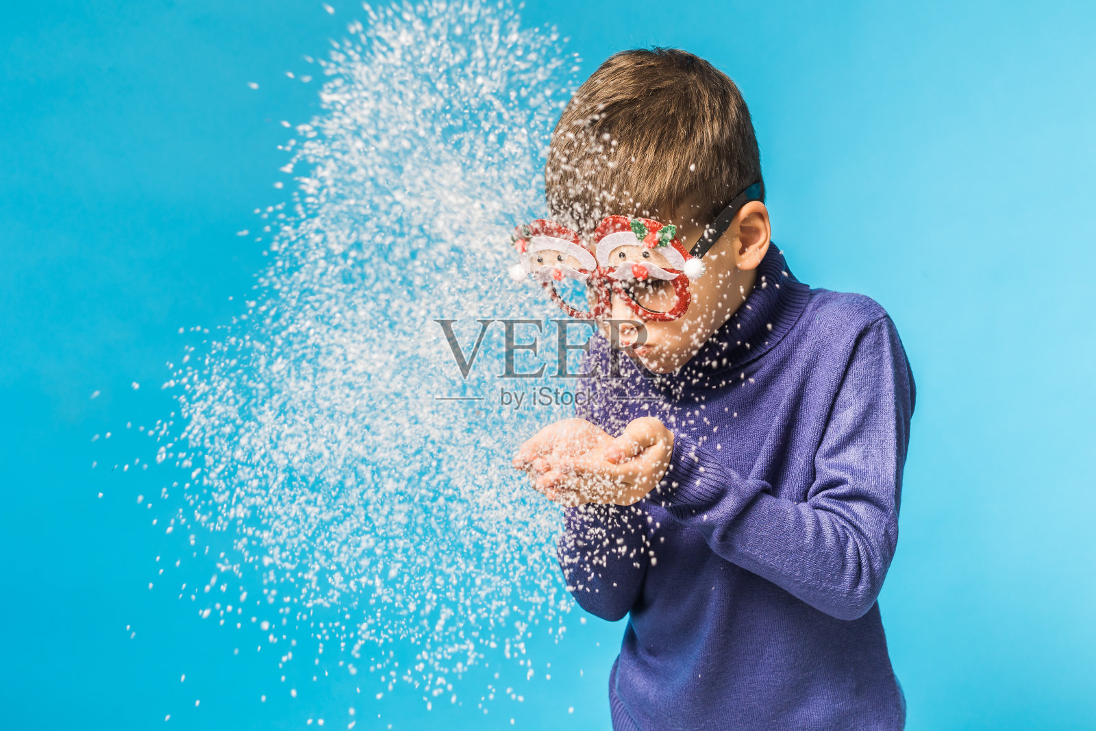 小男孩在蓝色的背景上吹着手中的雪。圣诞节和新年假期的概念。阿尔法一代和阿尔法一代的孩子照片摄影图片