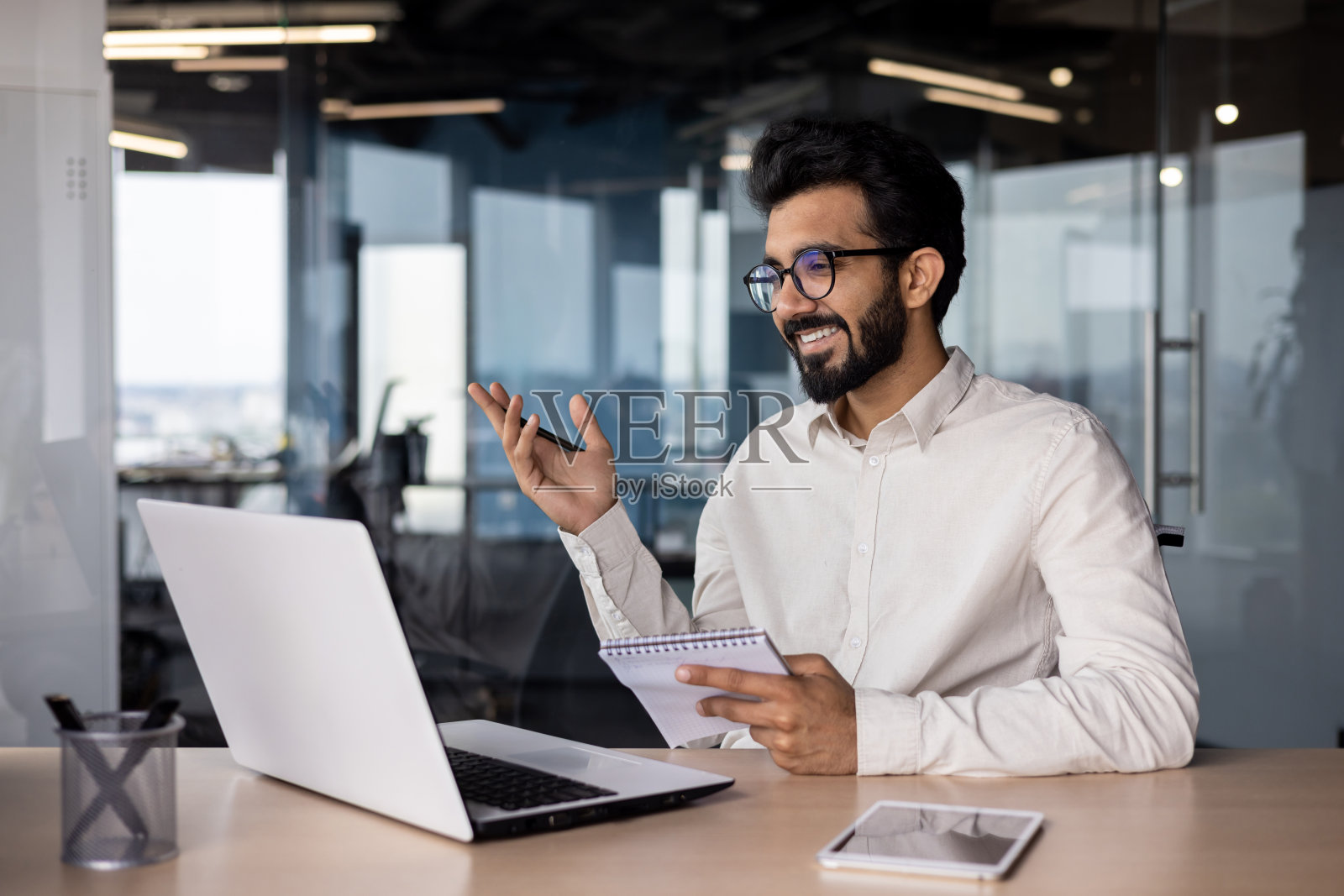 微笑的年轻印度男商人举行视频会议，通过笔记本电脑视频通话在线工作会议。他说话，用手做手势照片摄影图片