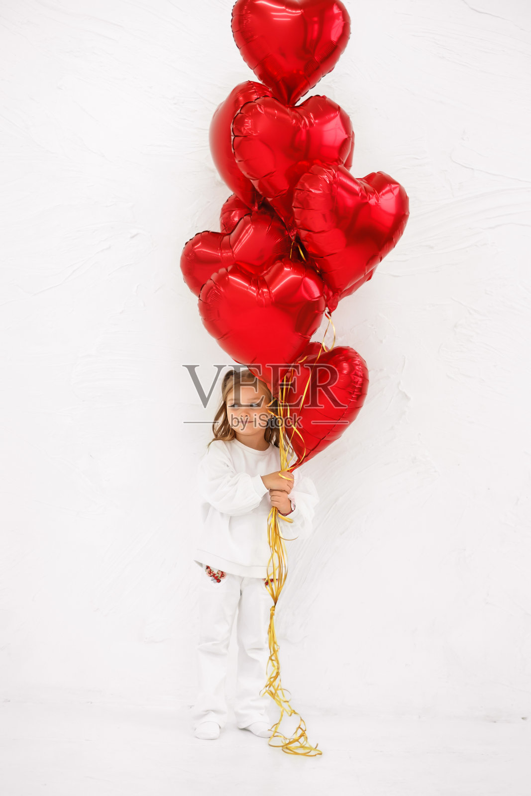 一个漂亮的女孩拿着一大束心形的红色箔球。照片摄影图片