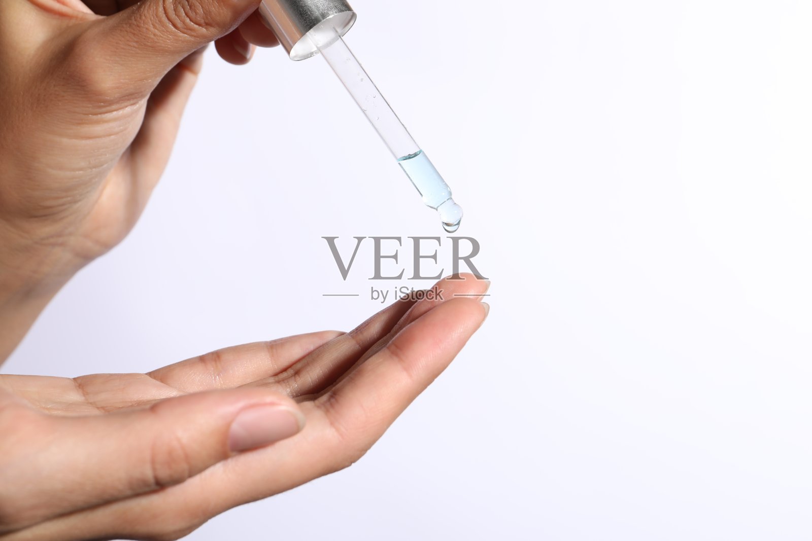 在白色背景上，一个女人在手指上涂化妆品精华液，特写。文本空间照片摄影图片