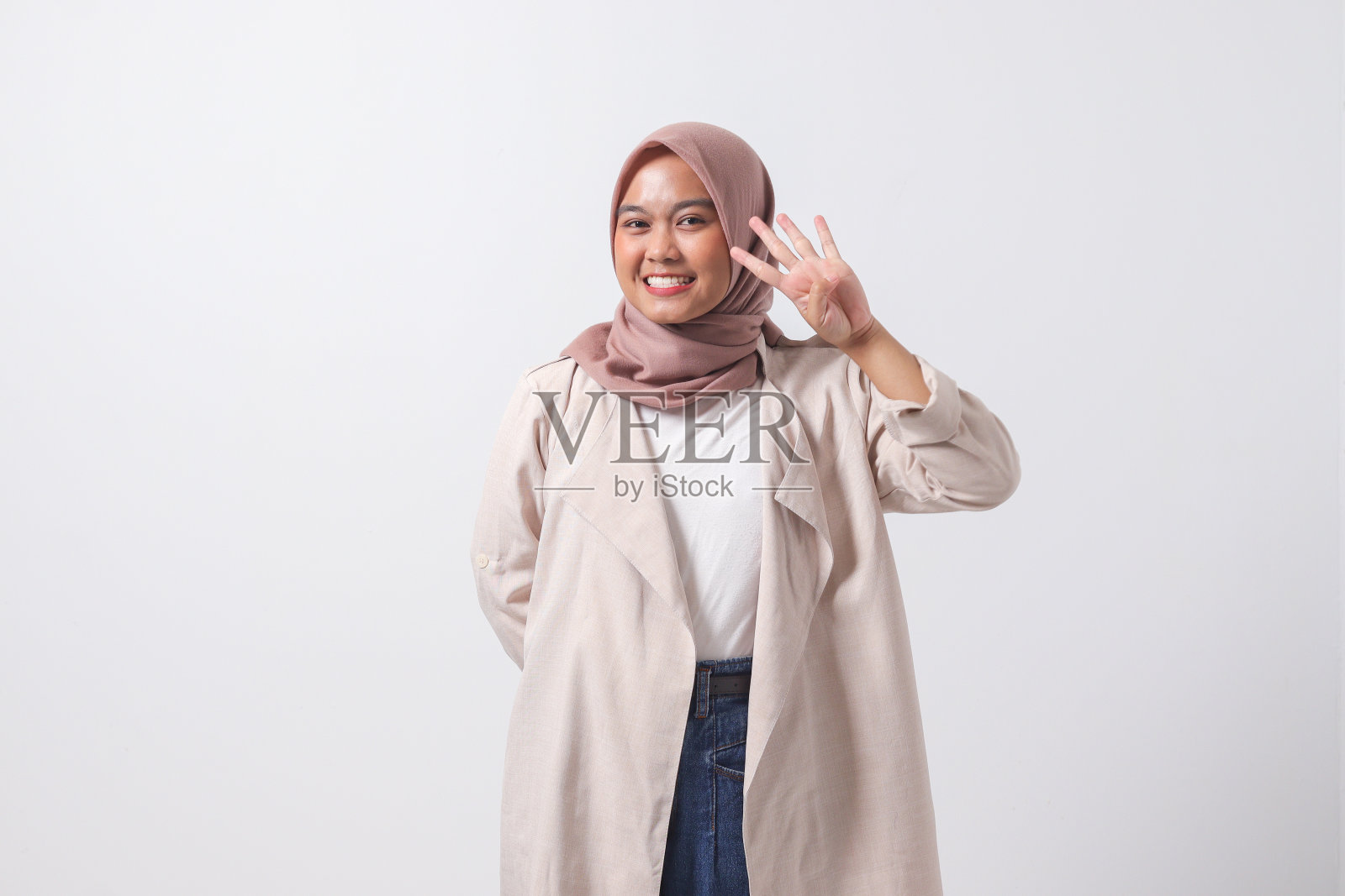 穿着休闲西装的亚洲头巾妇女的肖像，露出并指着第四根手指，同时微笑着自信和快乐。商人的概念。白色背景上的孤立图像照片摄影图片