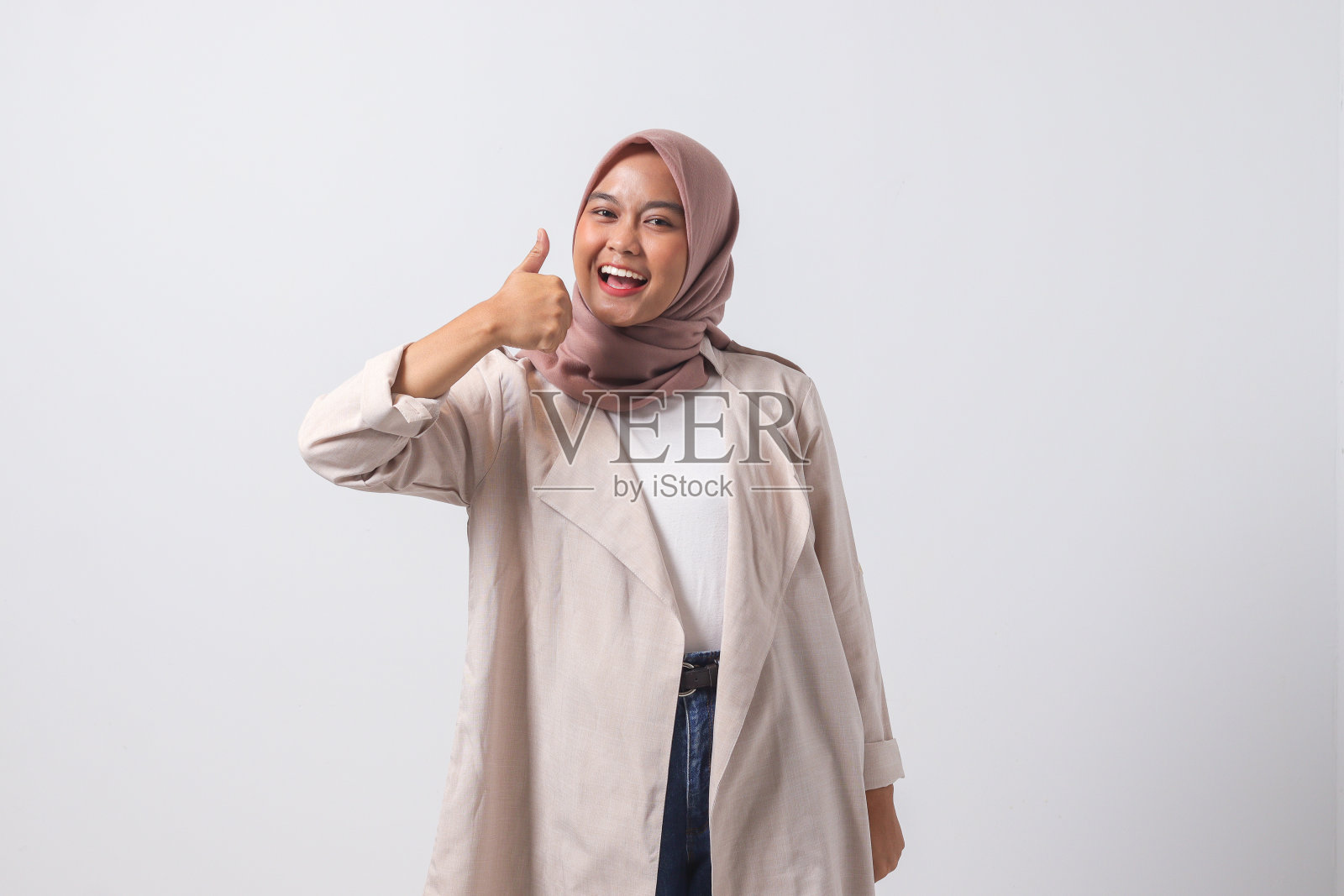一个穿着休闲套装，戴着头巾的迷人亚洲女性的肖像，她竖起大拇指，说着“干得好”。商人的概念。白色背景上的孤立图像照片摄影图片