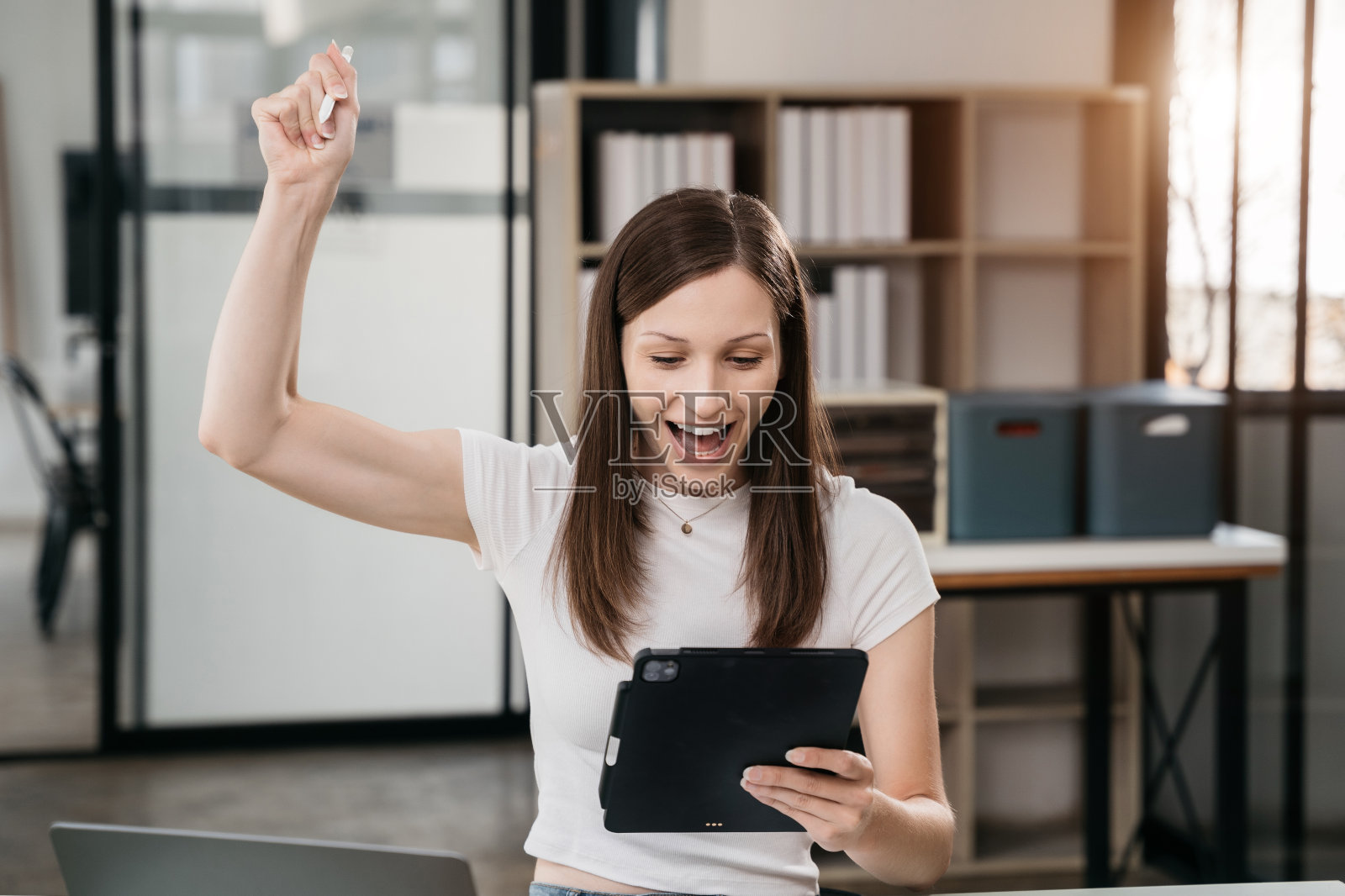 喜出望外的迷人兴奋的白人女性商务女工作者使用智能手机和笔记本电脑在办公室工作，感觉很快乐。照片摄影图片