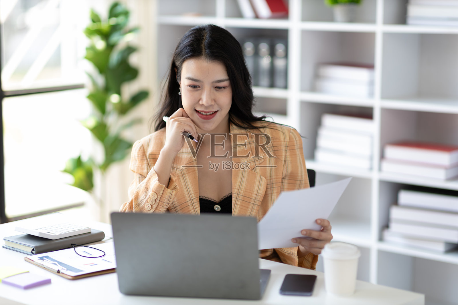 迷人的亚洲女商务秘书，在办公室里用笔记本电脑和文书工作。照片摄影图片