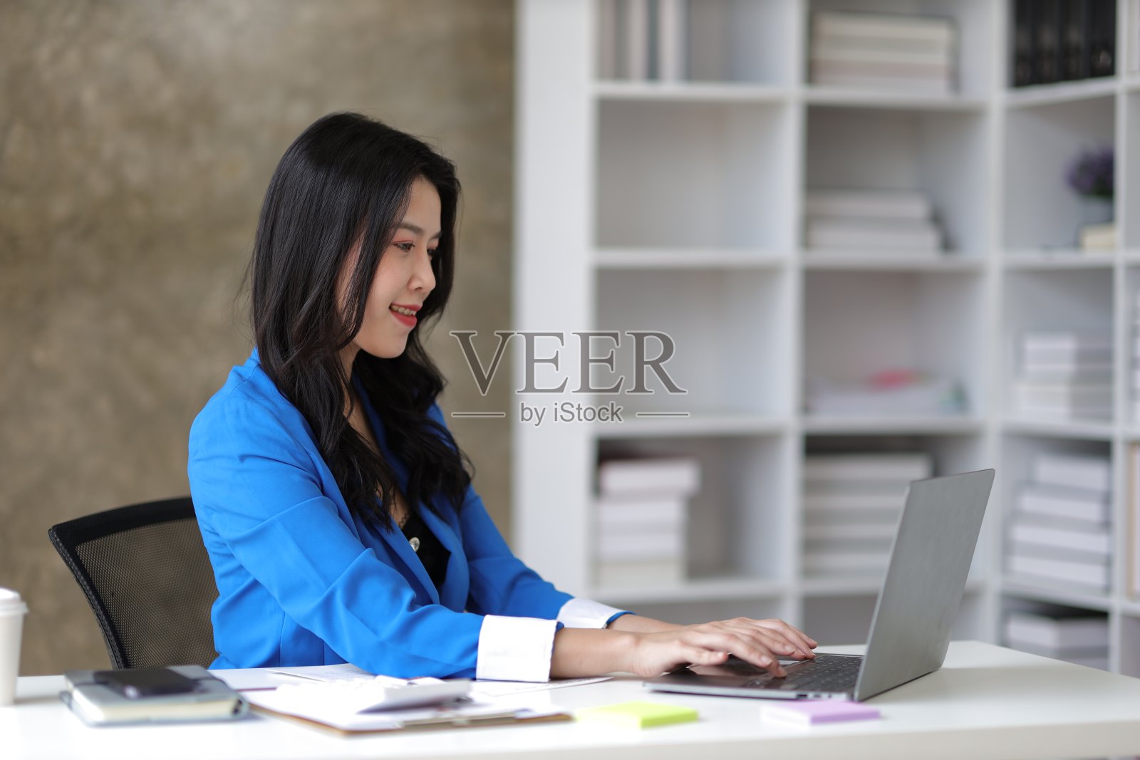 迷人的亚洲女商务秘书，在办公室里用笔记本电脑和文书工作。照片摄影图片