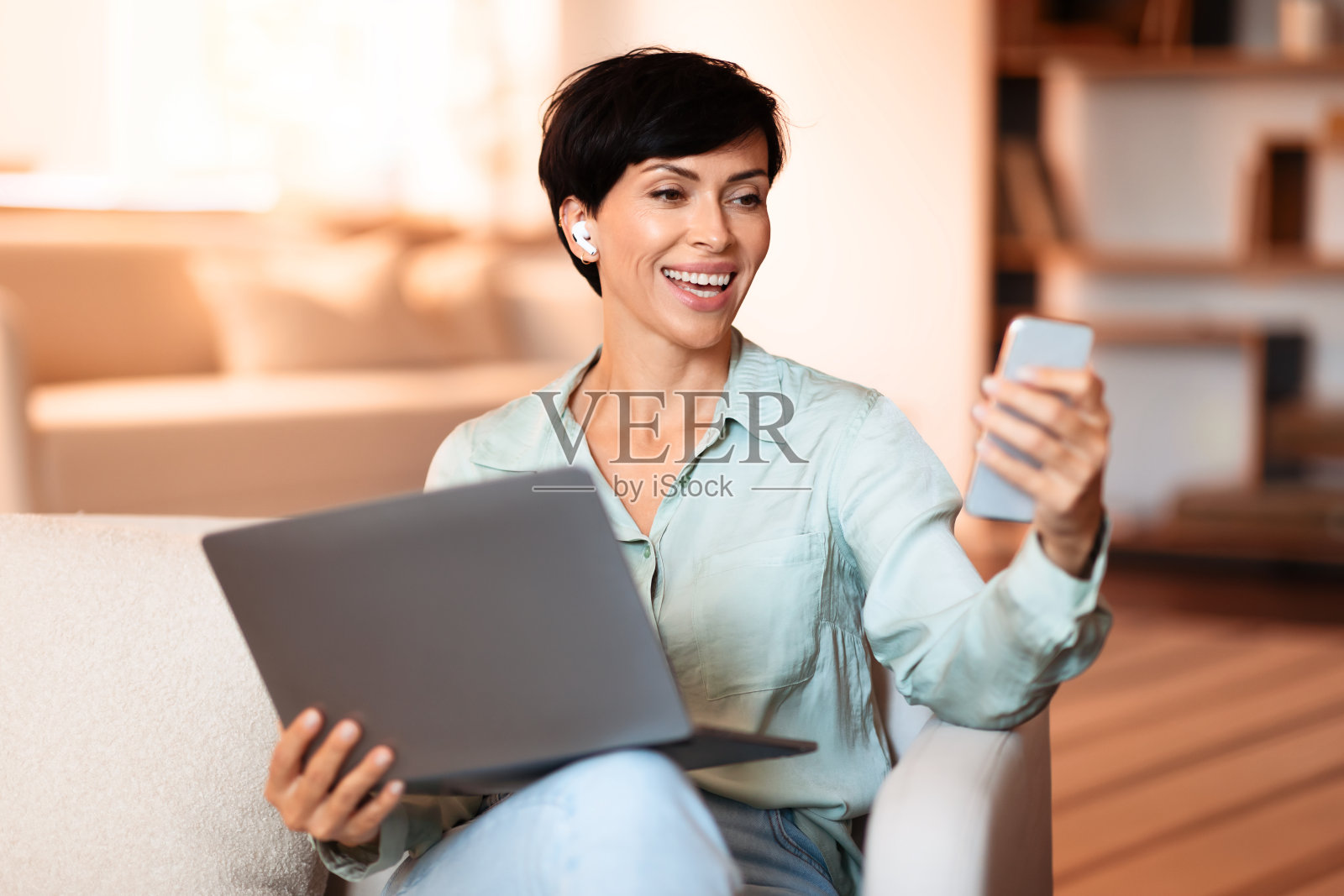 戴着耳机的女人在室内悠闲地浏览着手机和笔记本电脑照片摄影图片