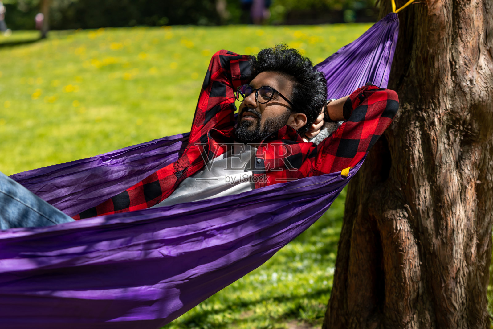 印度年轻人躺在吊床上，在公园里享受一天照片摄影图片