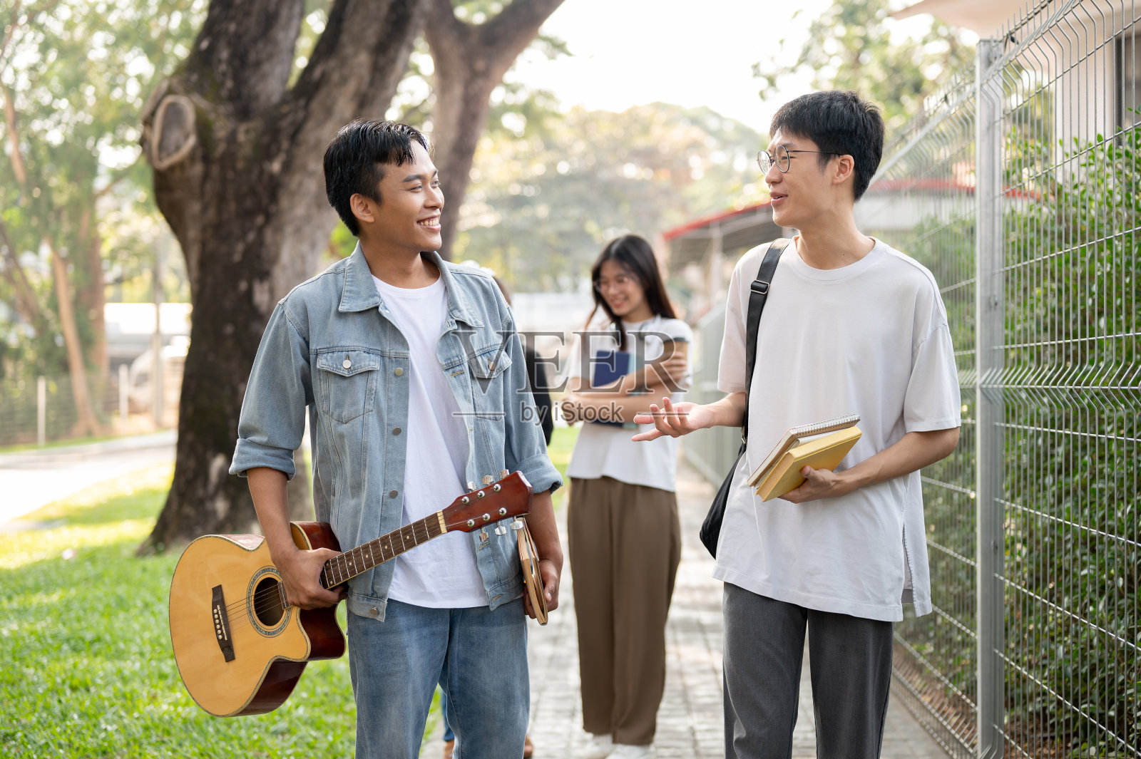 两个亚洲男同学正在校园的人行道上聊天。照片摄影图片