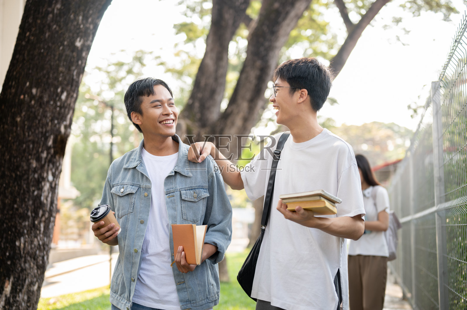 两个年轻的亚洲男性好朋友正在校园的人行道上聊天。照片摄影图片