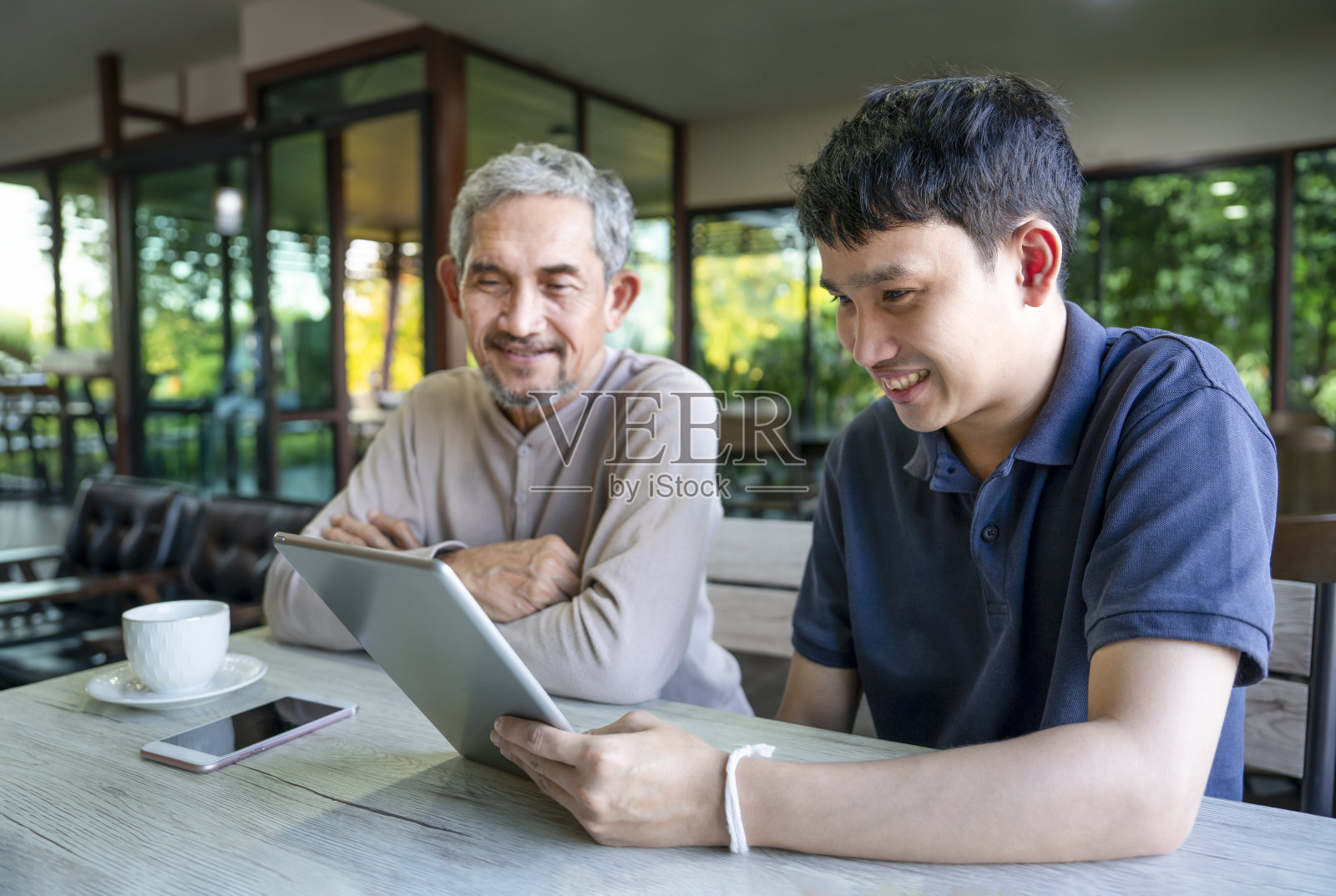 年轻的成年儿子和年长的父亲在咖啡馆用平板电脑与家人交流照片摄影图片