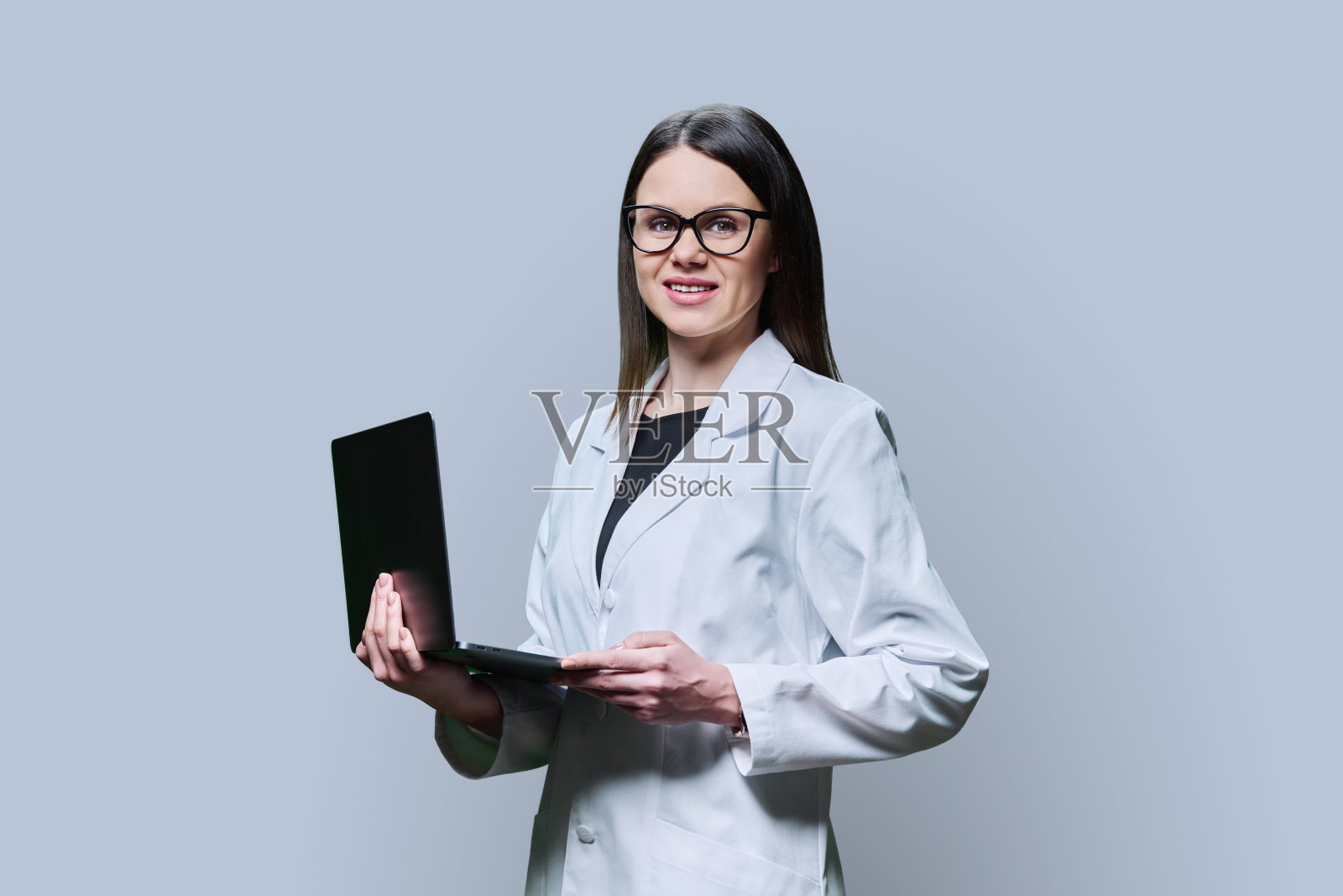 穿白大褂的女医学家，药剂师用灰色背景的笔记本电脑照片摄影图片