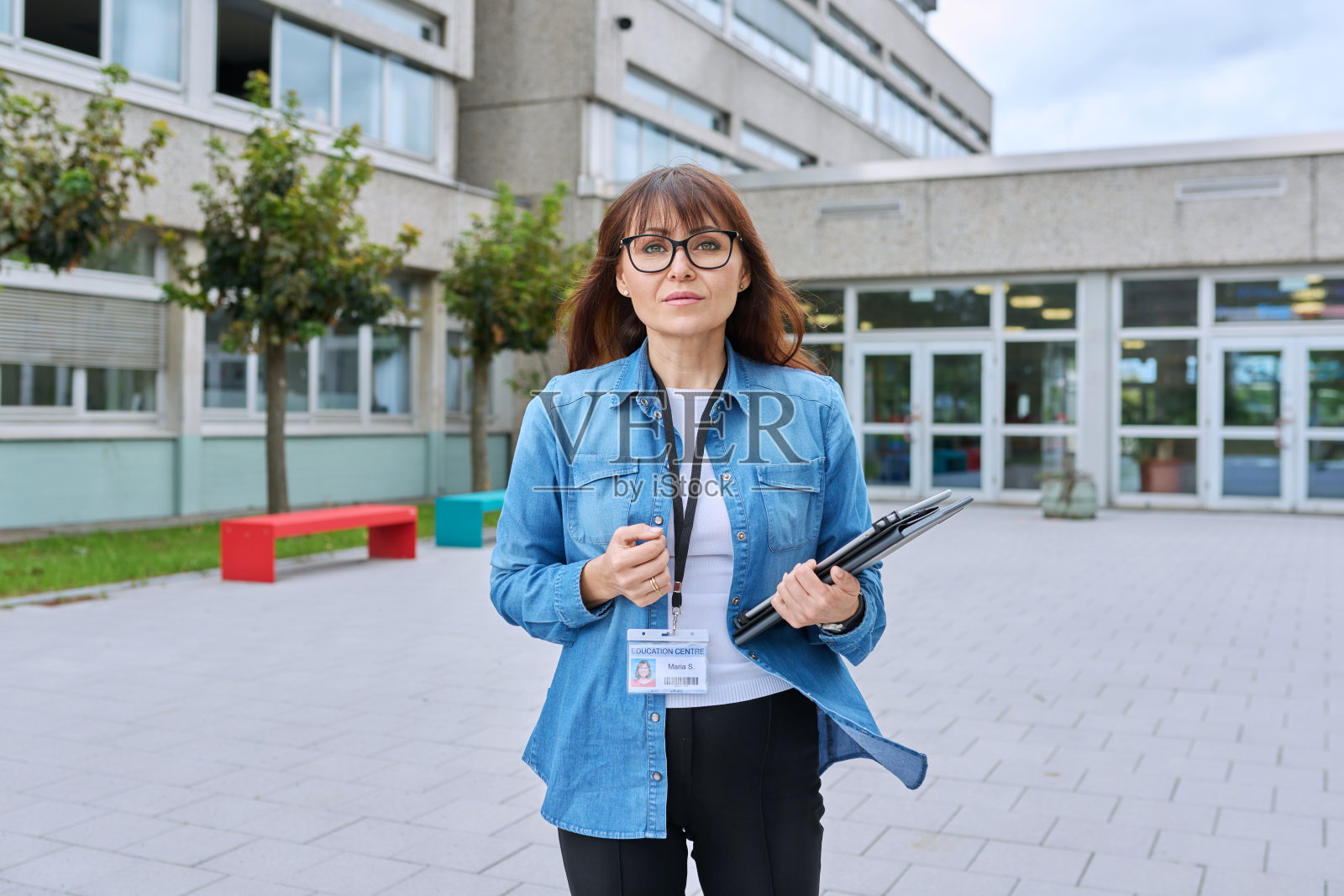 手持数码平板电脑的中年女教师在学校大楼附近摆姿势照片摄影图片