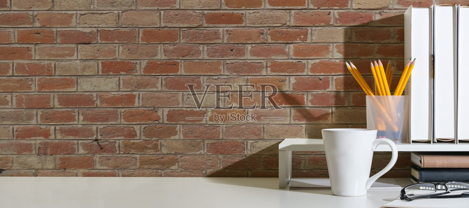 时尚的工作场所，白色的桌子上摆放着书籍、咖啡杯、相框和盆栽。为你的文本复制空间。照片摄影图片