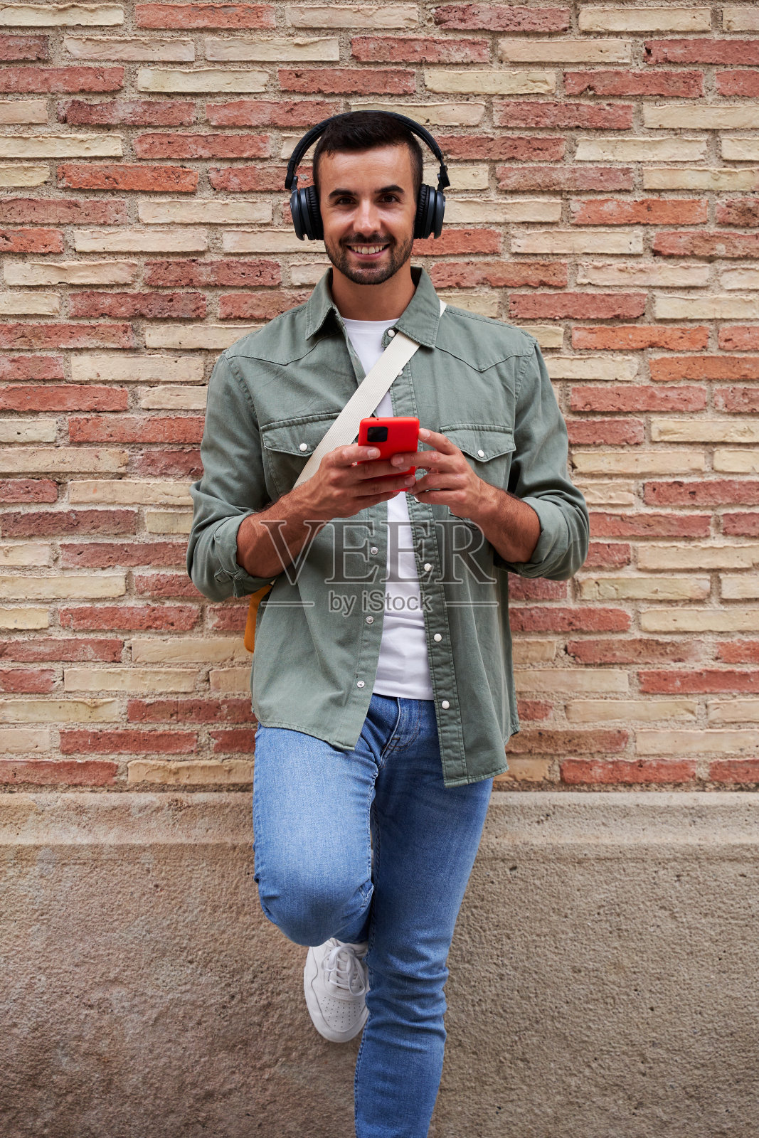 一名白人男子一边看镜头一边用手机发在线信息和听音乐。照片摄影图片