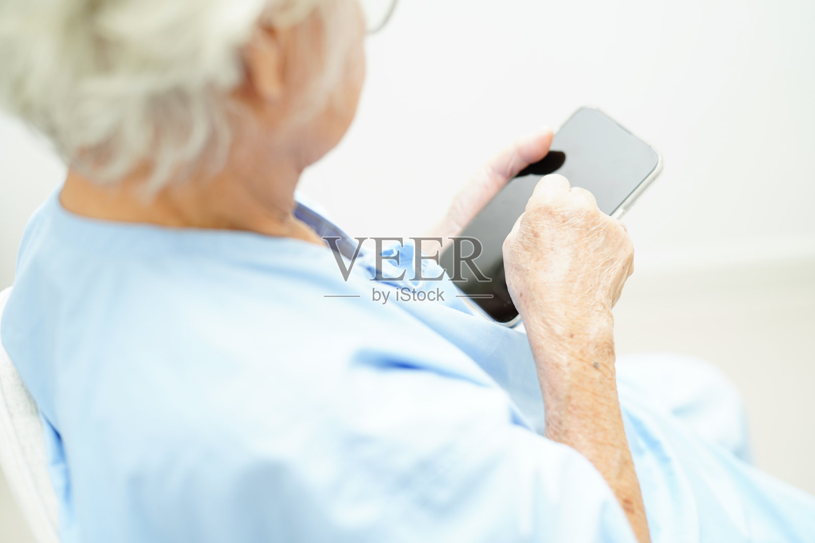 佩戴眼镜或视觉眼镜的亚洲老年女性使用智能手机进行居家护理服务。照片摄影图片