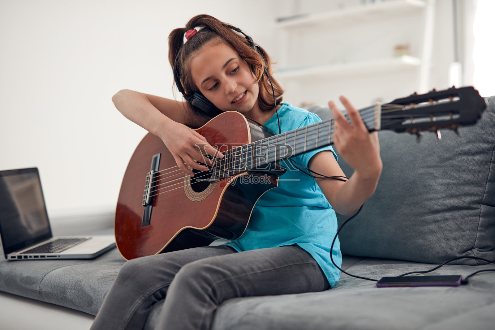 孩子一边弹吉他一边用笔记本电脑看视频课程。照片摄影图片