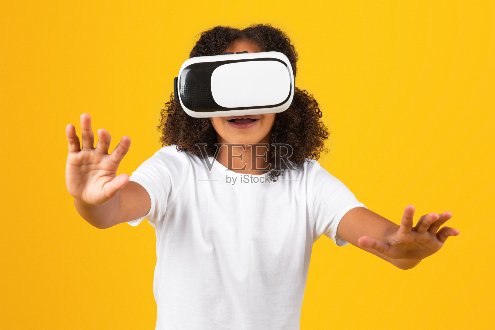 又惊又喜的黑人少女穿着白色t恤，戴着VR眼镜享受空闲时间，用手玩网络游戏照片摄影图片