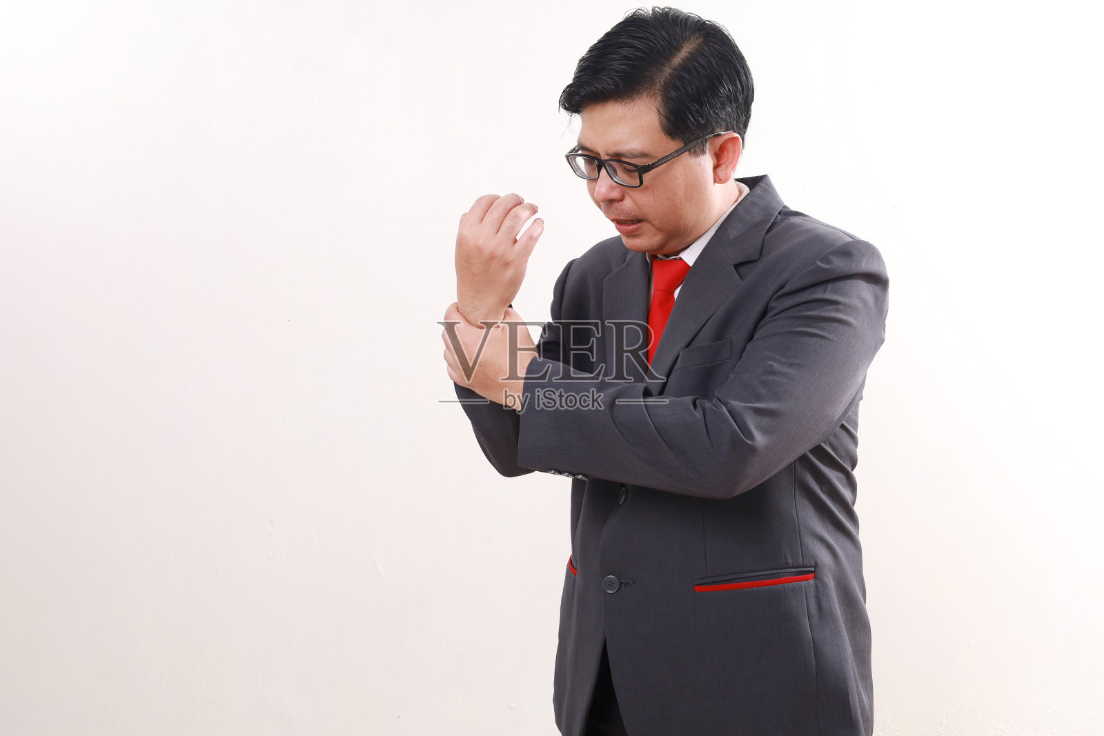 一个亚洲商人站在那里，手里握着他抽筋的手腕。隔离在白色背景上照片摄影图片