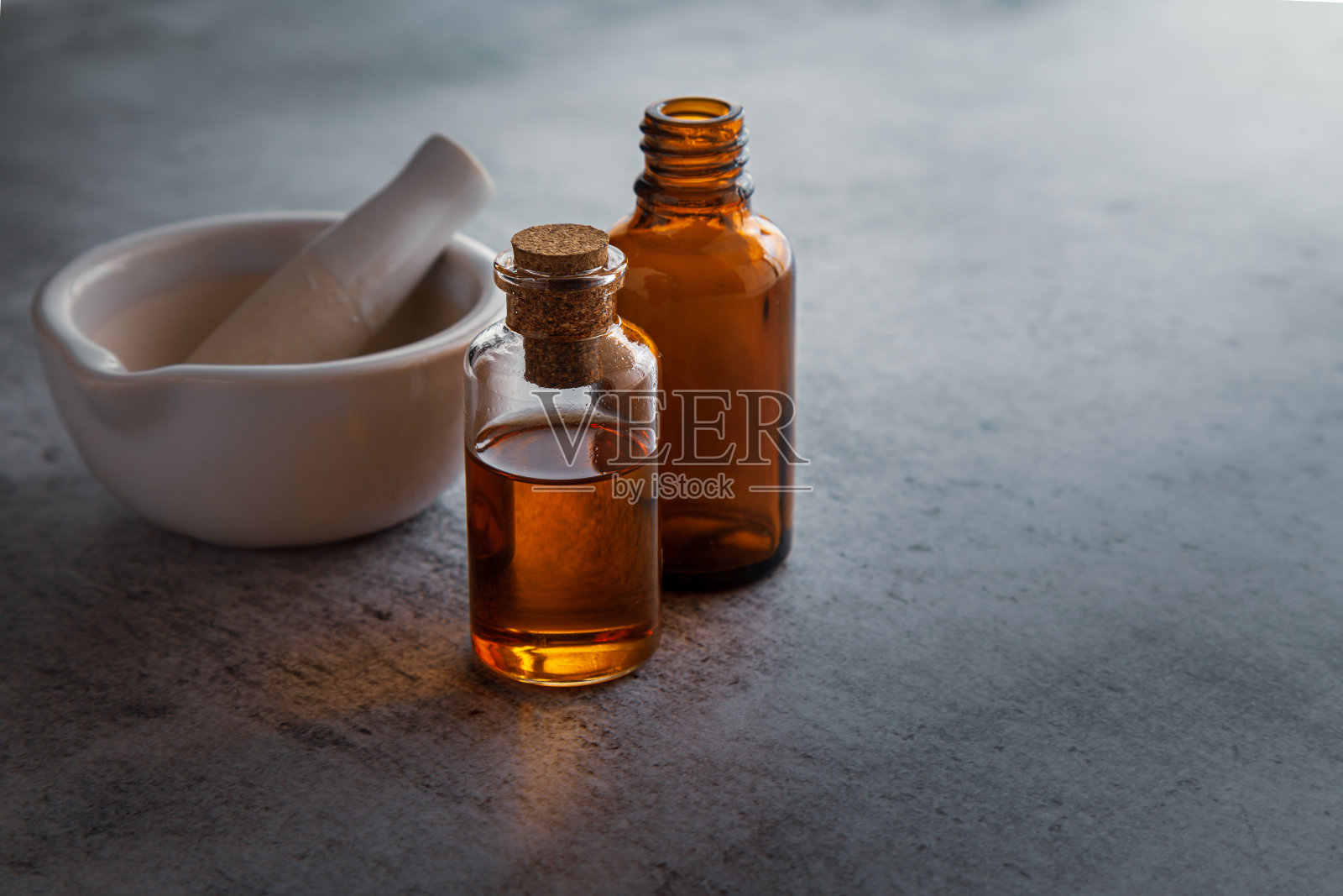 用研钵和研杵盛有深橙色精油的圆形玻璃瓶。照片摄影图片