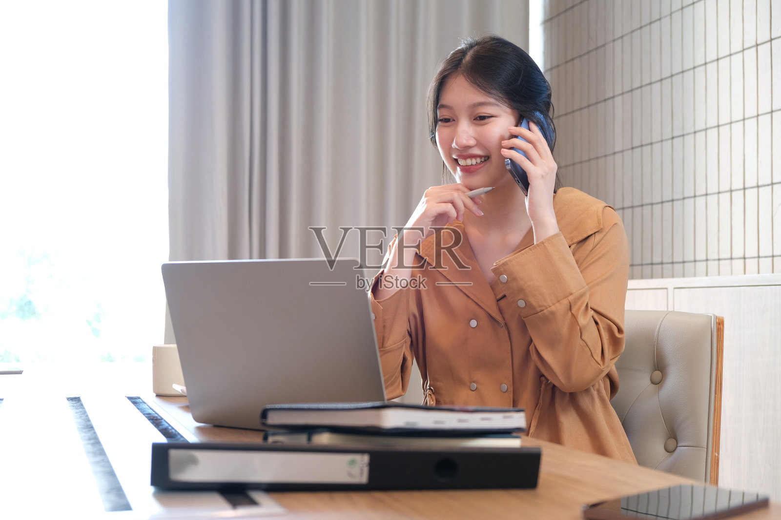 漂亮的女商人坐在办公桌前用智能手机和笔记本电脑工作，在家工作的概念照片摄影图片