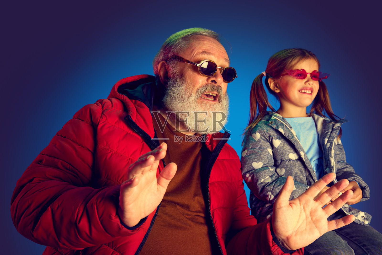 时尚的老人和小女孩，孩子看电视，足球比赛，电影在蓝色背景的霓虹灯照片摄影图片