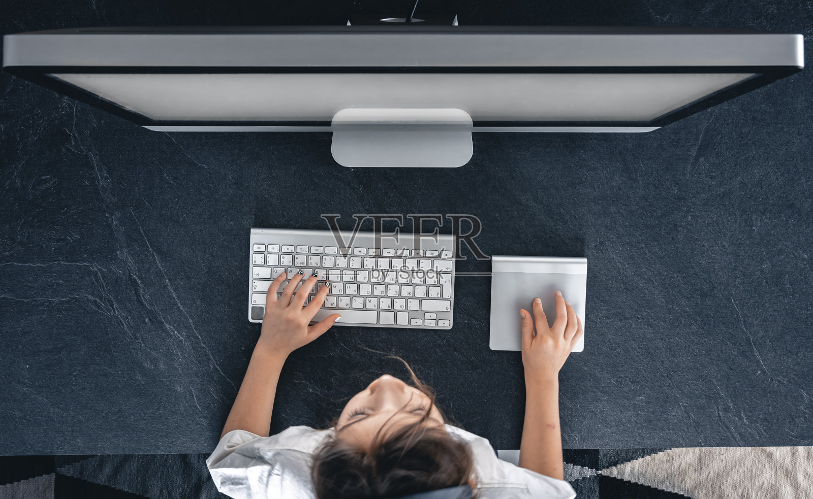 一个小女孩坐在电脑屏幕前的桌子上，俯视图。照片摄影图片