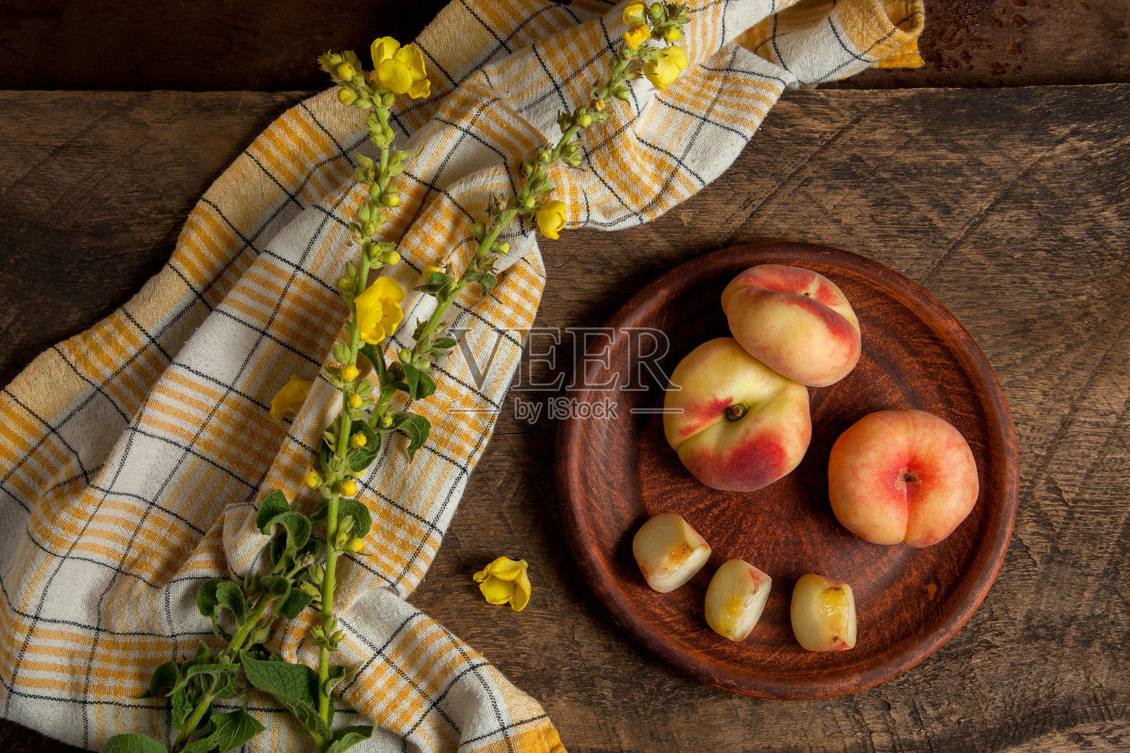 粘土板与切割和整个土星桃子或扁桃子木制背景与黄色厨房毛巾。照片摄影图片