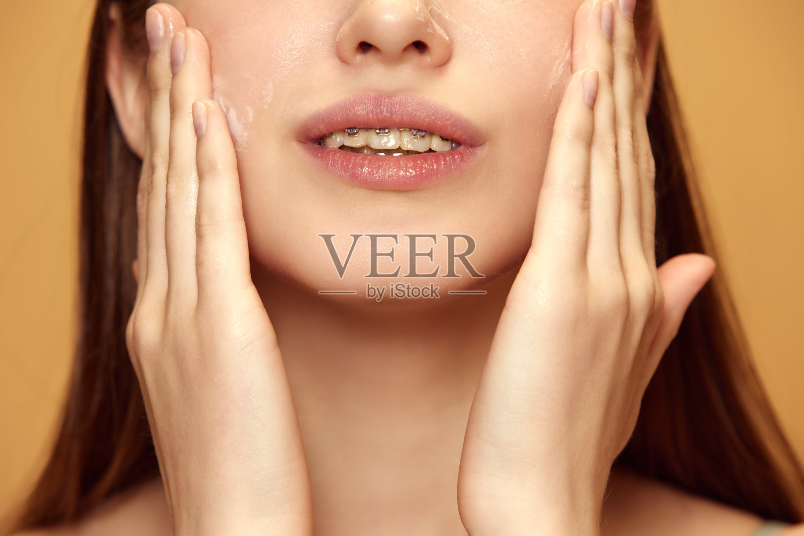 在米色背景下，年轻女子用面霜涂抹面部皮肤，以保持其健康和容光焕发的外观。照片摄影图片