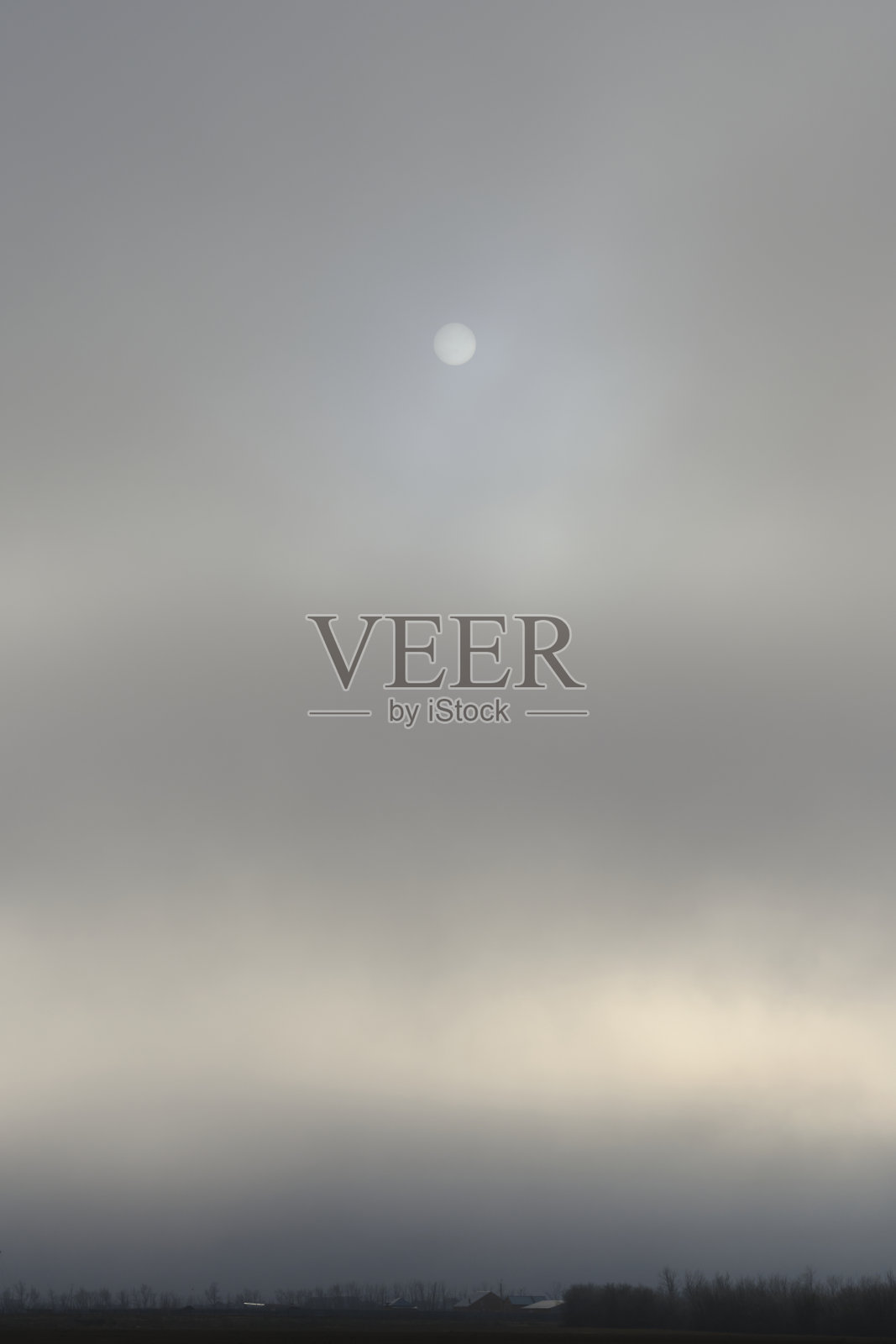 村庄的房子在雾的背景，雾蒙蒙的天空与暗淡的太阳。照片摄影图片